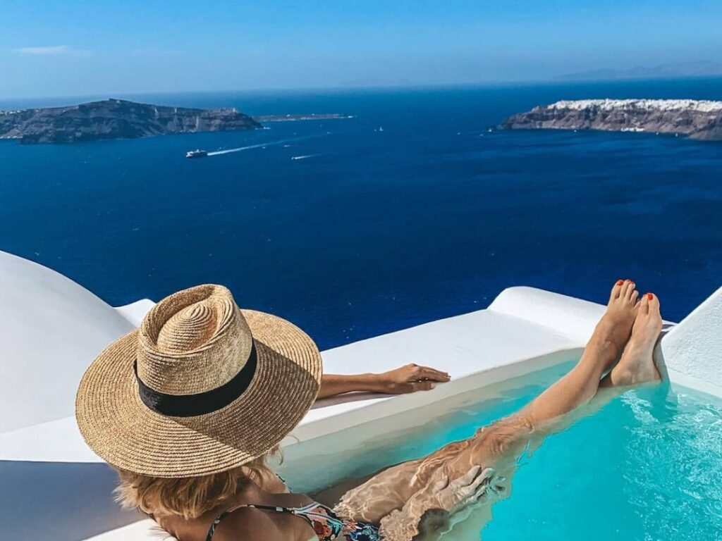 woman wearing a hat relaxing at infinity pool on caldera of santorini greece